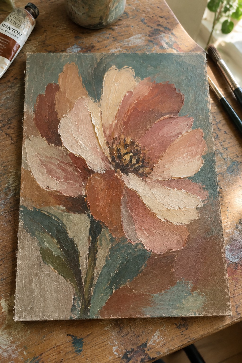 Impasto flower painting in earthy pinks and browns beside paint tube on wooden table